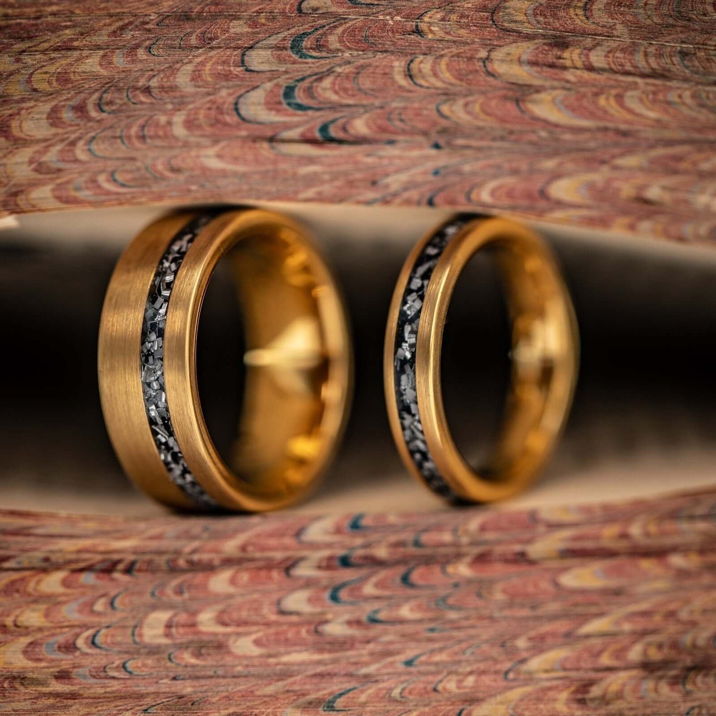 Mens and womens yellow gold meteorite rings next to each other between pages of a book