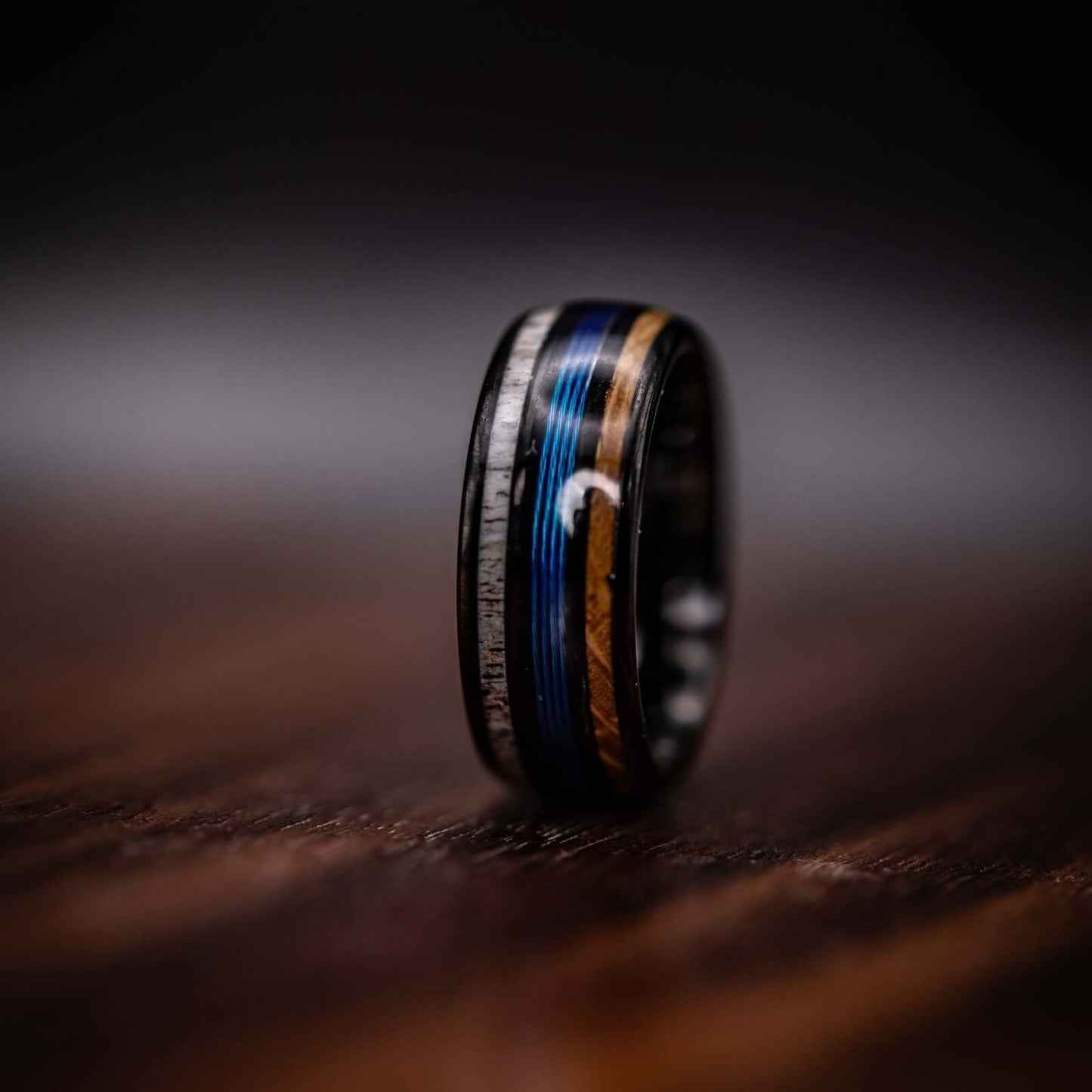 Handcrafted fishing wedding ring showcasing antler, whiskey barrel wood, and blue line accents.