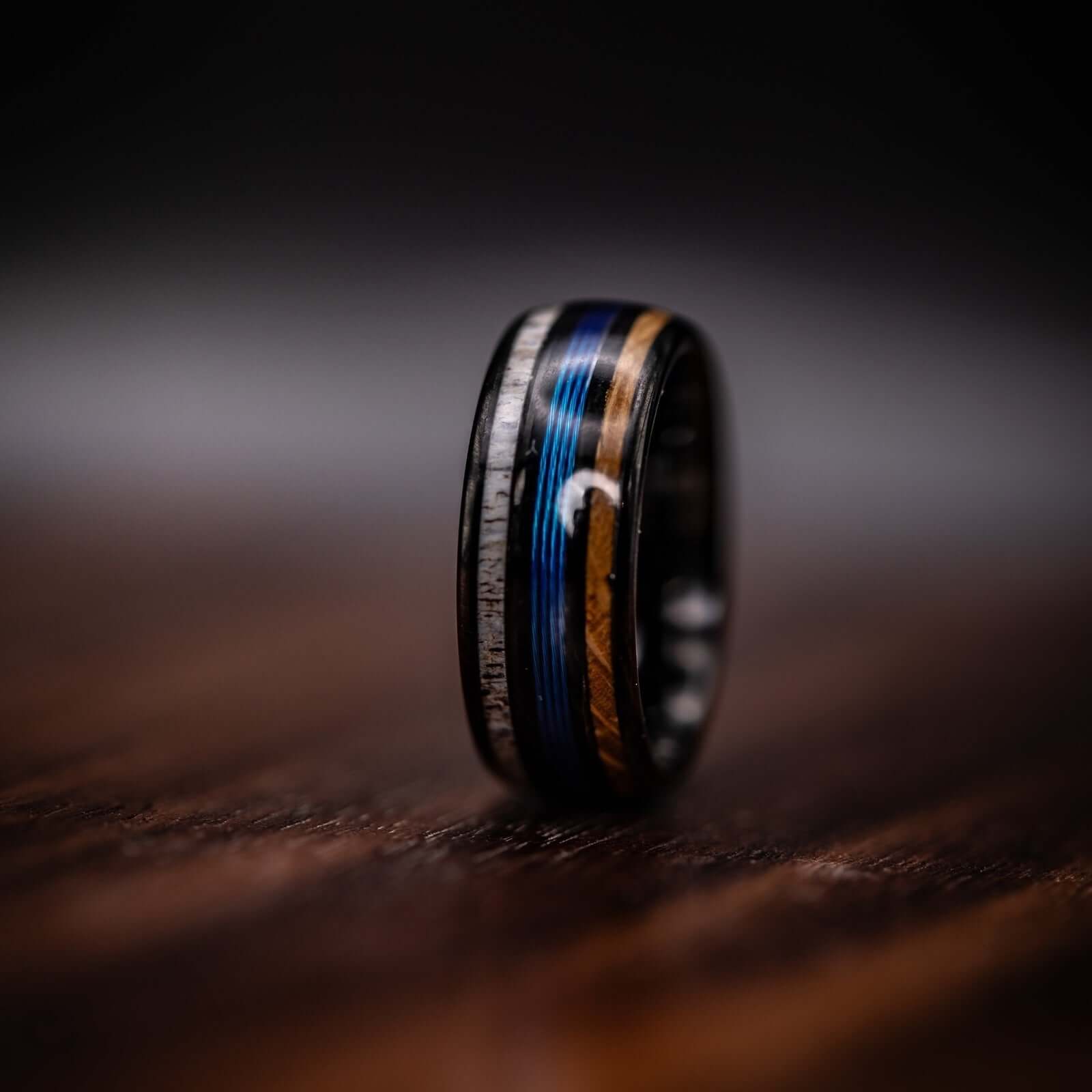 Handcrafted fishing wedding ring showcasing antler, whiskey barrel wood, and blue line accents.