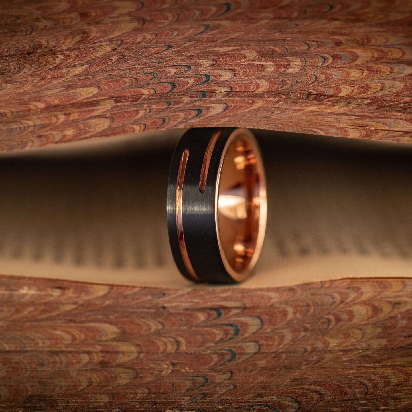 Black and rose gold wedding band nestled between vintage book pages, showcasing unique design and craftsmanship.