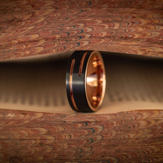 Black and rose gold wedding band nestled between vintage book pages, showcasing unique design and craftsmanship.