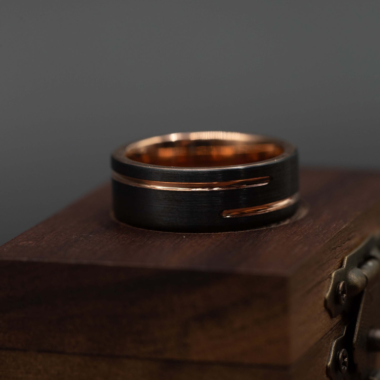 Black and rose gold wedding band on a wooden box, showcasing its unique 8mm design and tungsten carbide material.