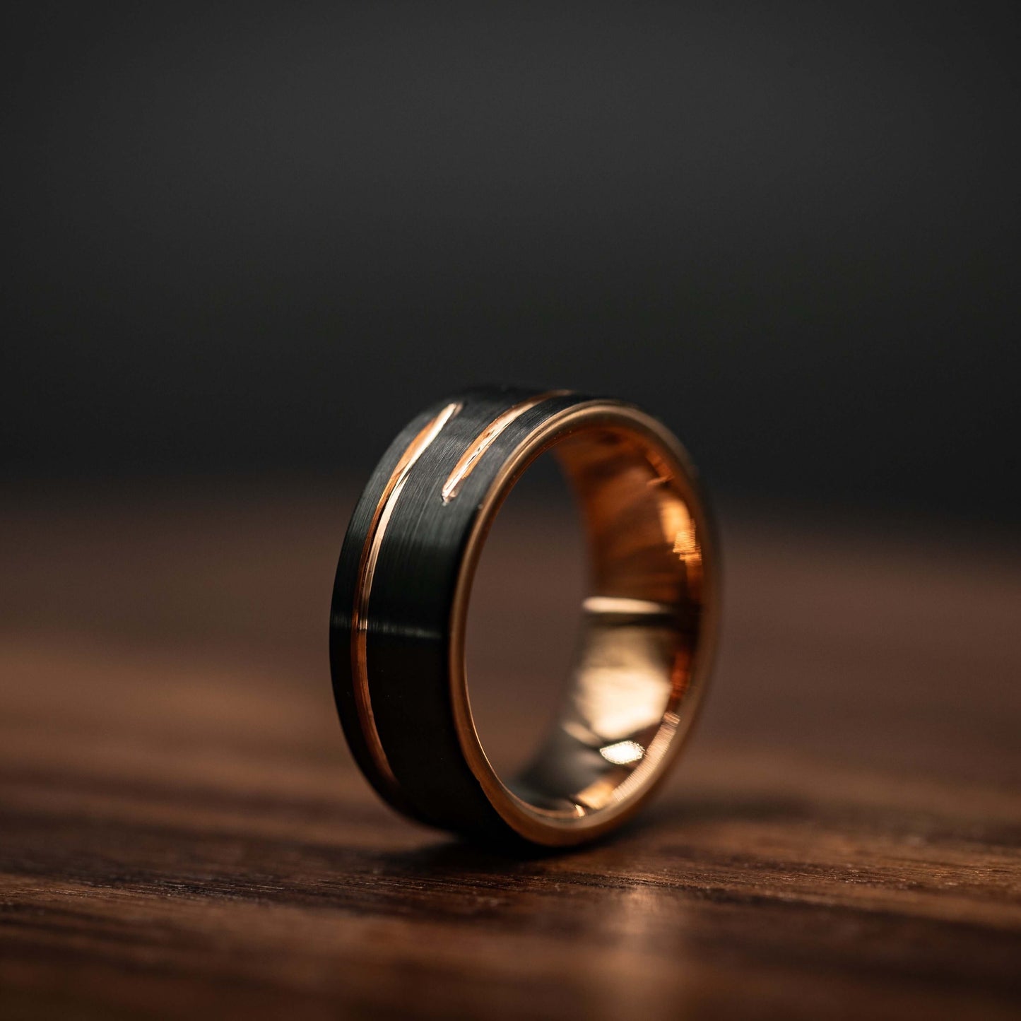 Black and rose gold 8mm tungsten carbide wedding band on wooden surface, highlighting unique design and durability.