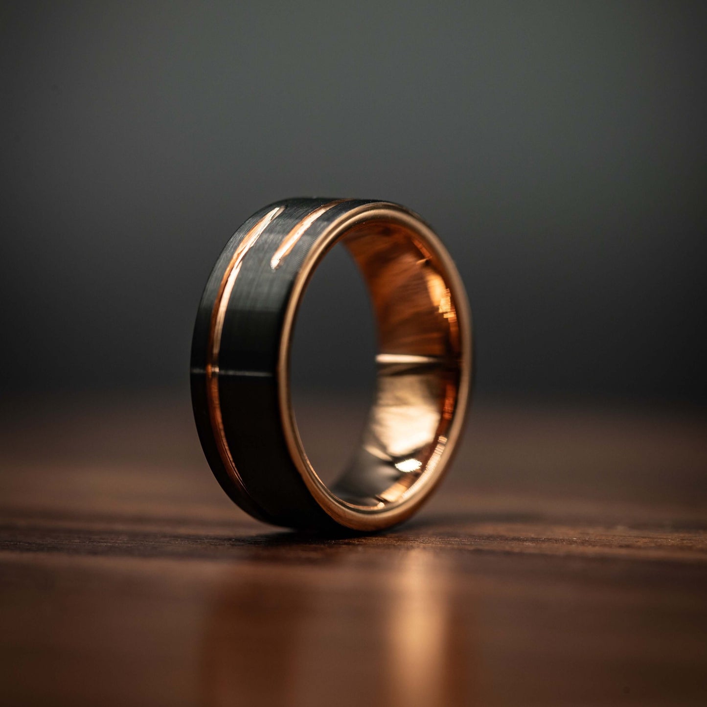Black and rose gold 8mm wedding band with unique offset inlay on wooden surface.