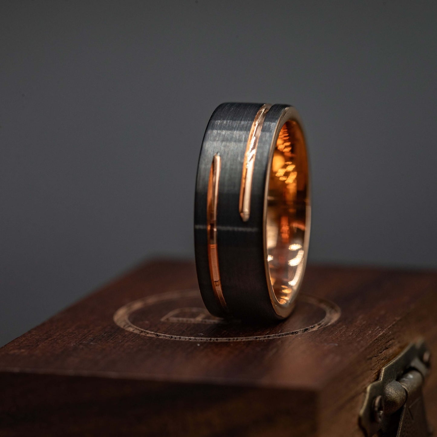 Black and rose gold 8mm wedding band, unique tungsten carbide ring on a wooden display.