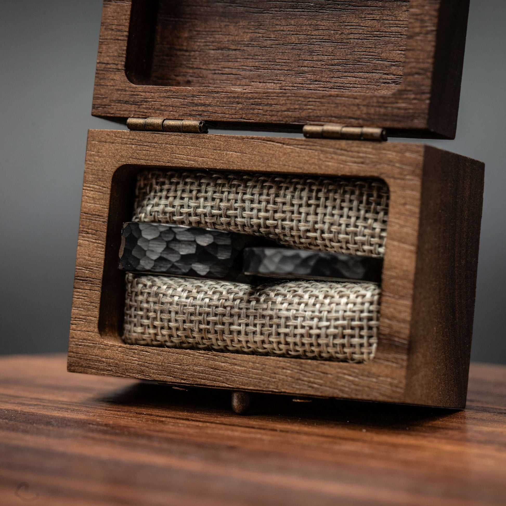 Black hammered tungsten wedding rings displayed in a wooden box with linen lining, showcasing a unique couples ring set.
