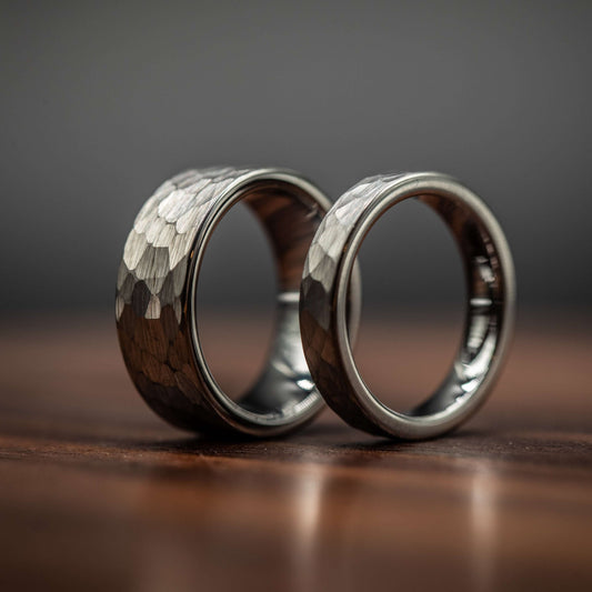 Hammered silver tungsten wedding rings set for couples, showcasing unique texture and durability on a wooden surface.