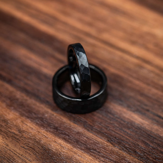 Black hammered tungsten wedding rings set for couples on a wooden surface. Perfect for his and hers.