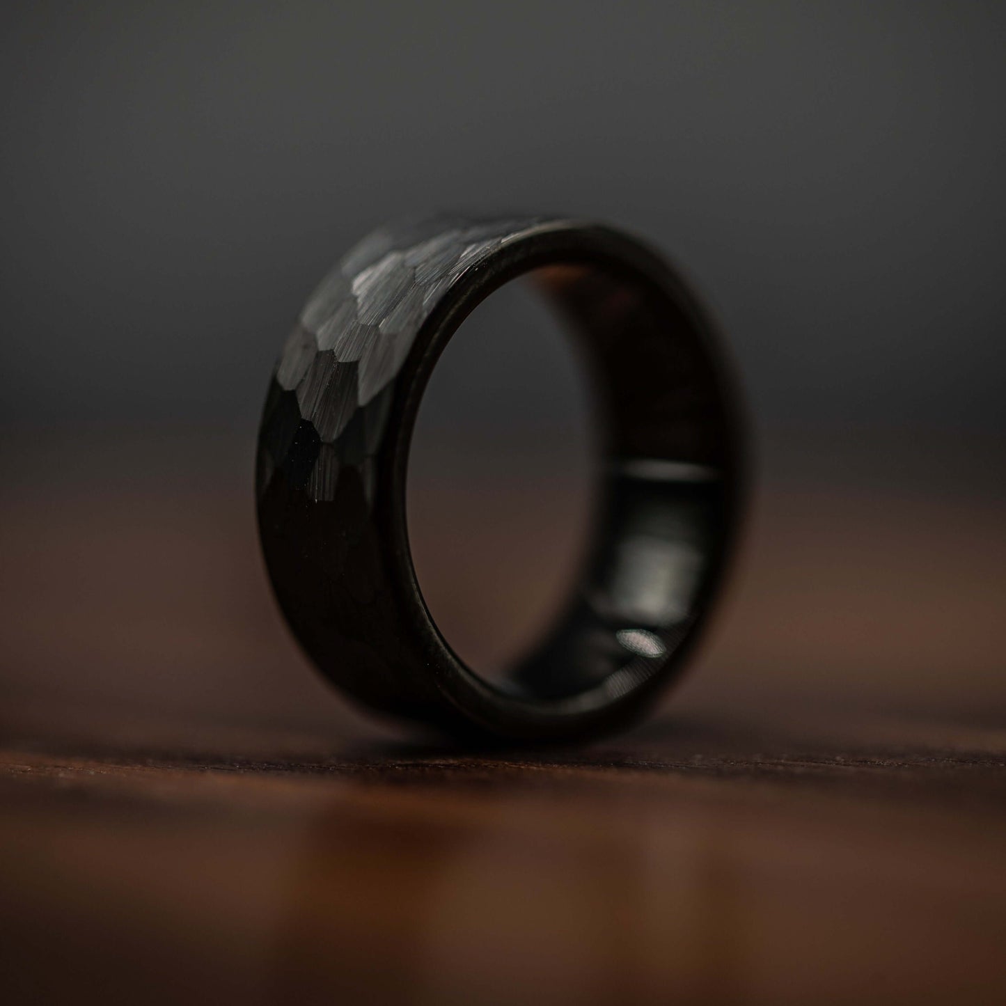 Hammered black tungsten wedding ring for men, showcasing bold design and durable craftsmanship on a wooden surface.