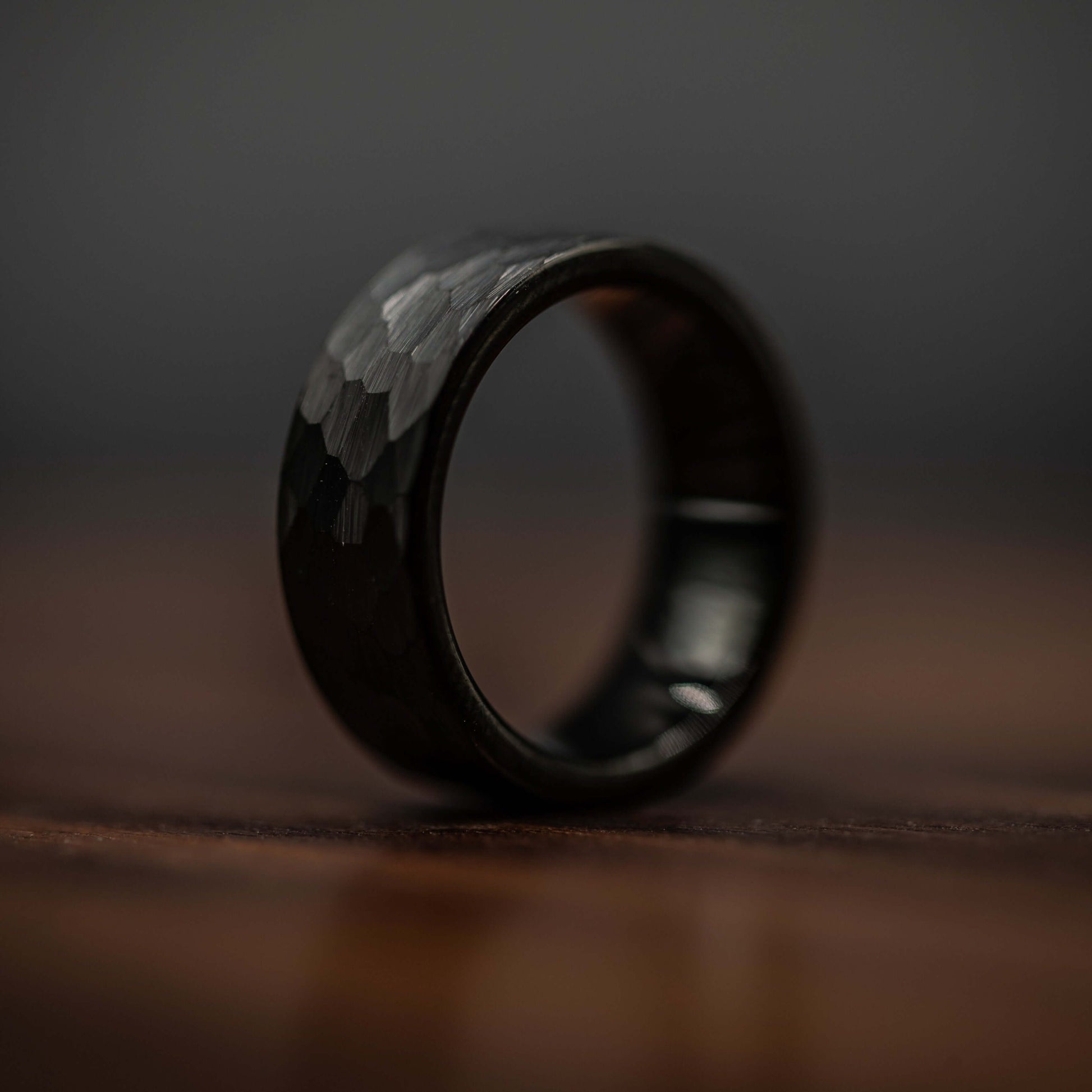 Hammered black tungsten wedding ring for men, showcasing bold design and durable craftsmanship on a wooden surface.