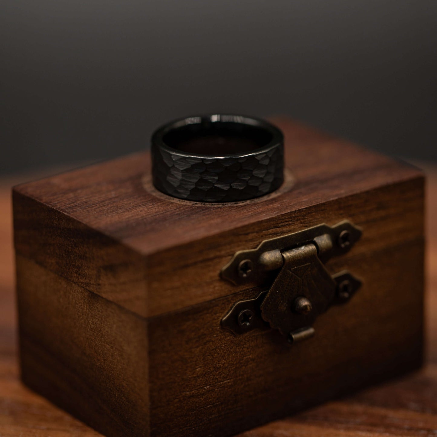 Hammered black tungsten wedding ring displayed on a rustic wooden box, showcasing its bold design and craftsmanship.