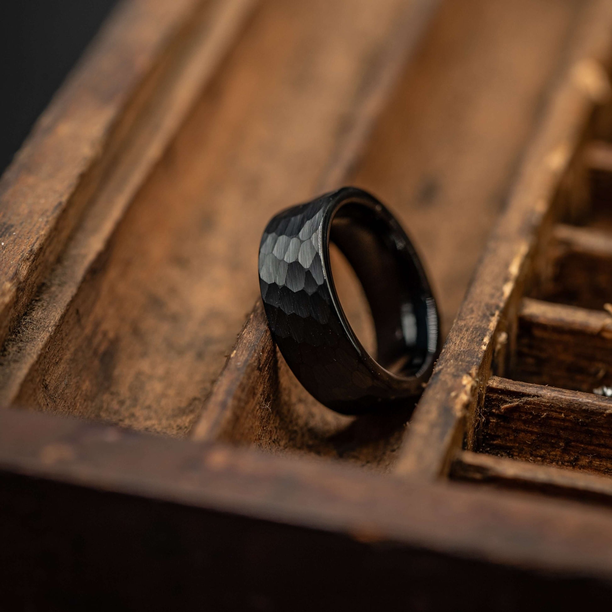 Black hammered tungsten wedding ring on a wooden display tray, showcasing its unique texture and durability.
