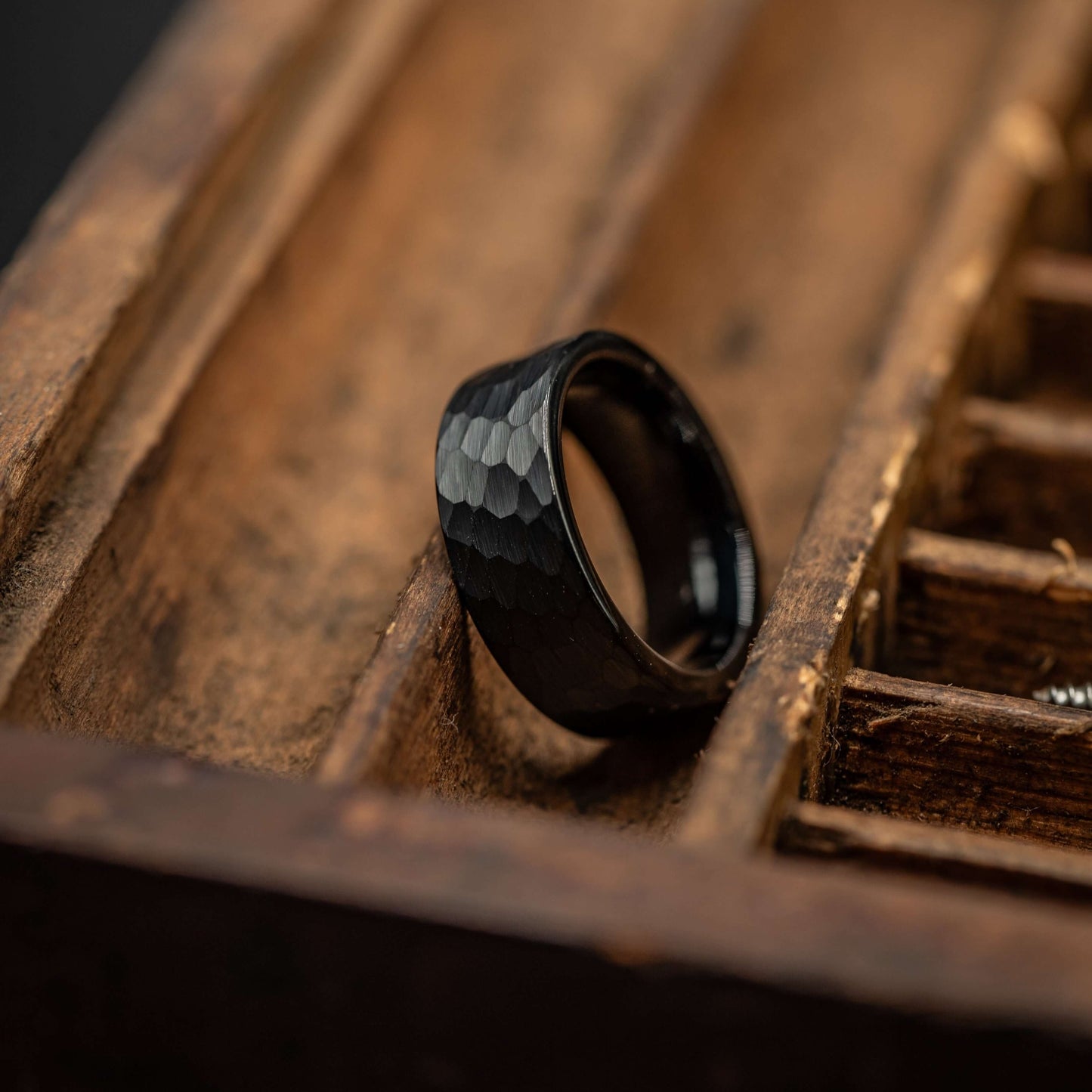 Hammered black tungsten wedding band resting on wooden display, showcasing its unique texture and durable design.