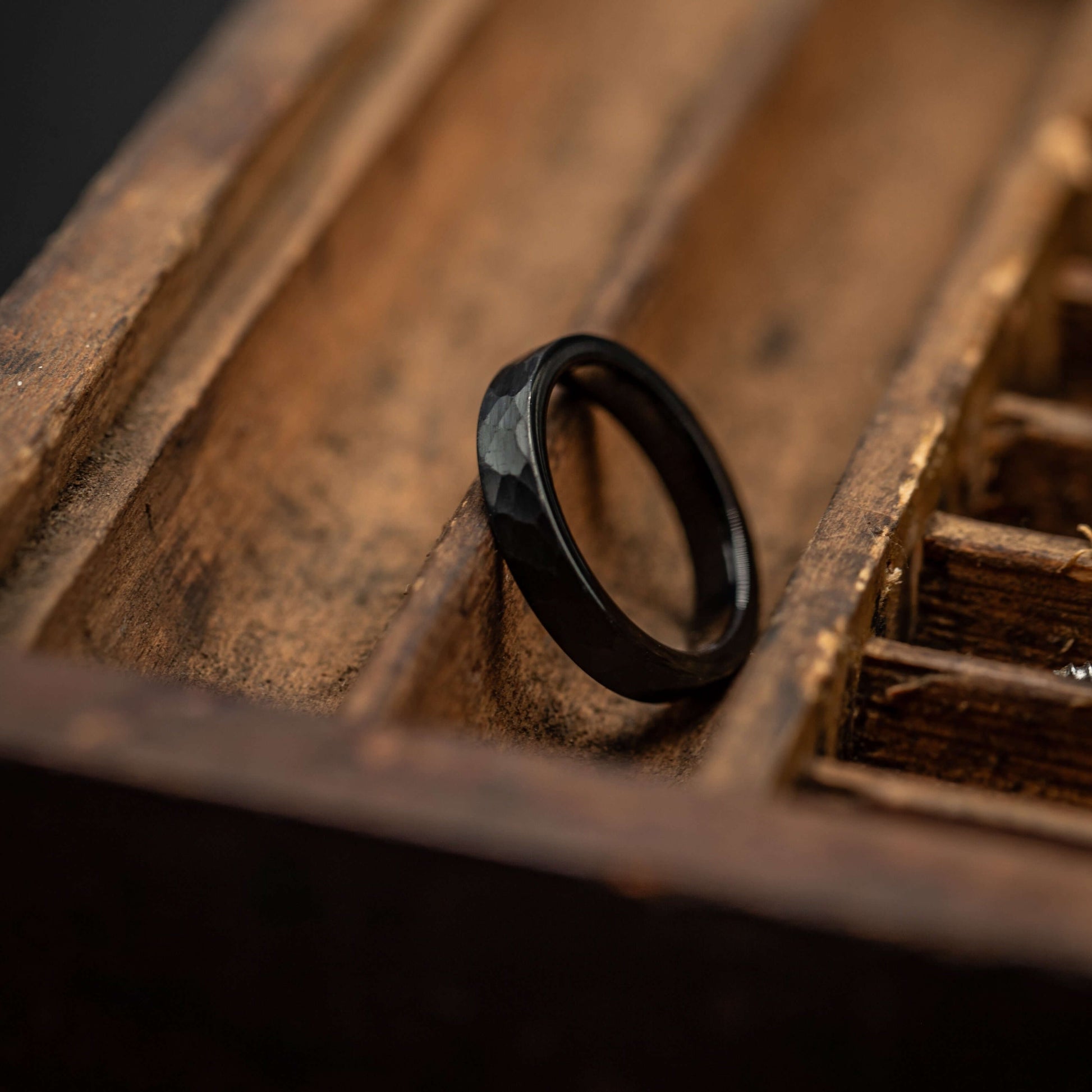 Black hammered tungsten wedding ring showcased in a vintage wooden box. Unique couples wedding band.