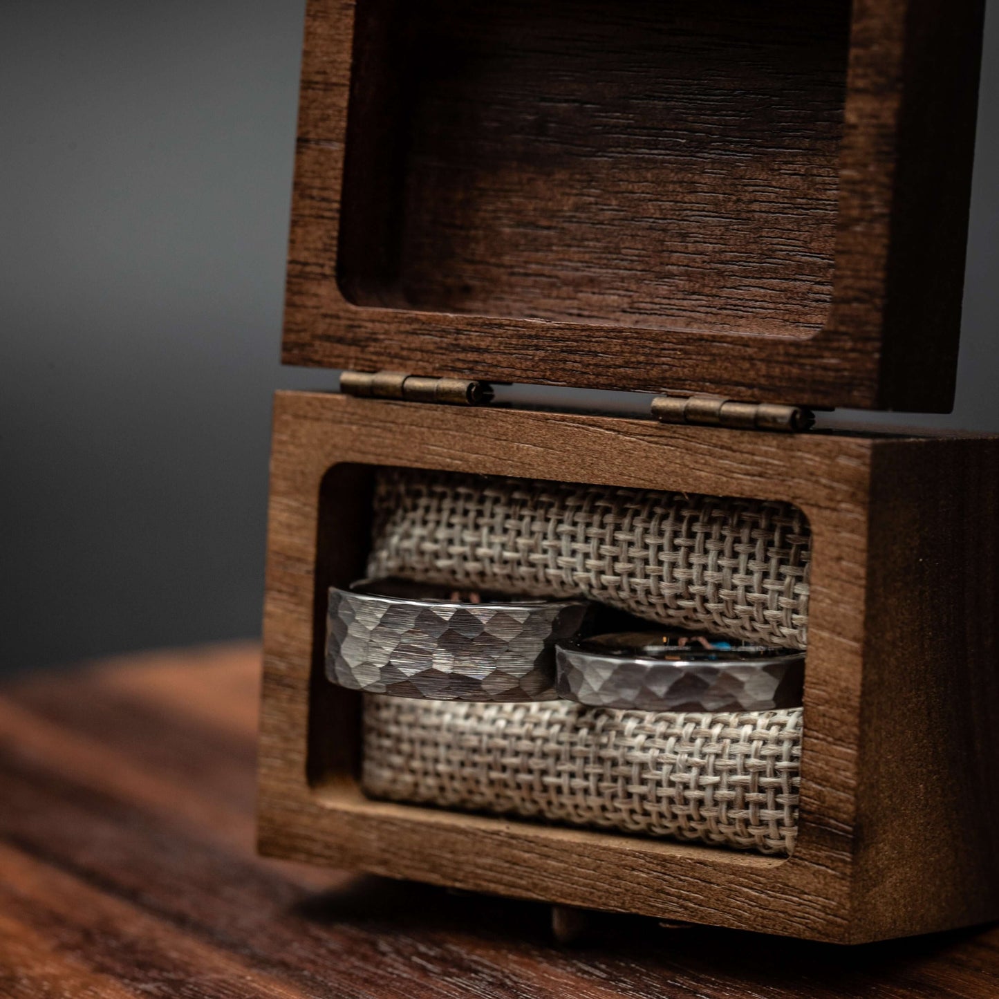Silver hammered tungsten wedding rings displayed in a rustic wooden box with linen lining.