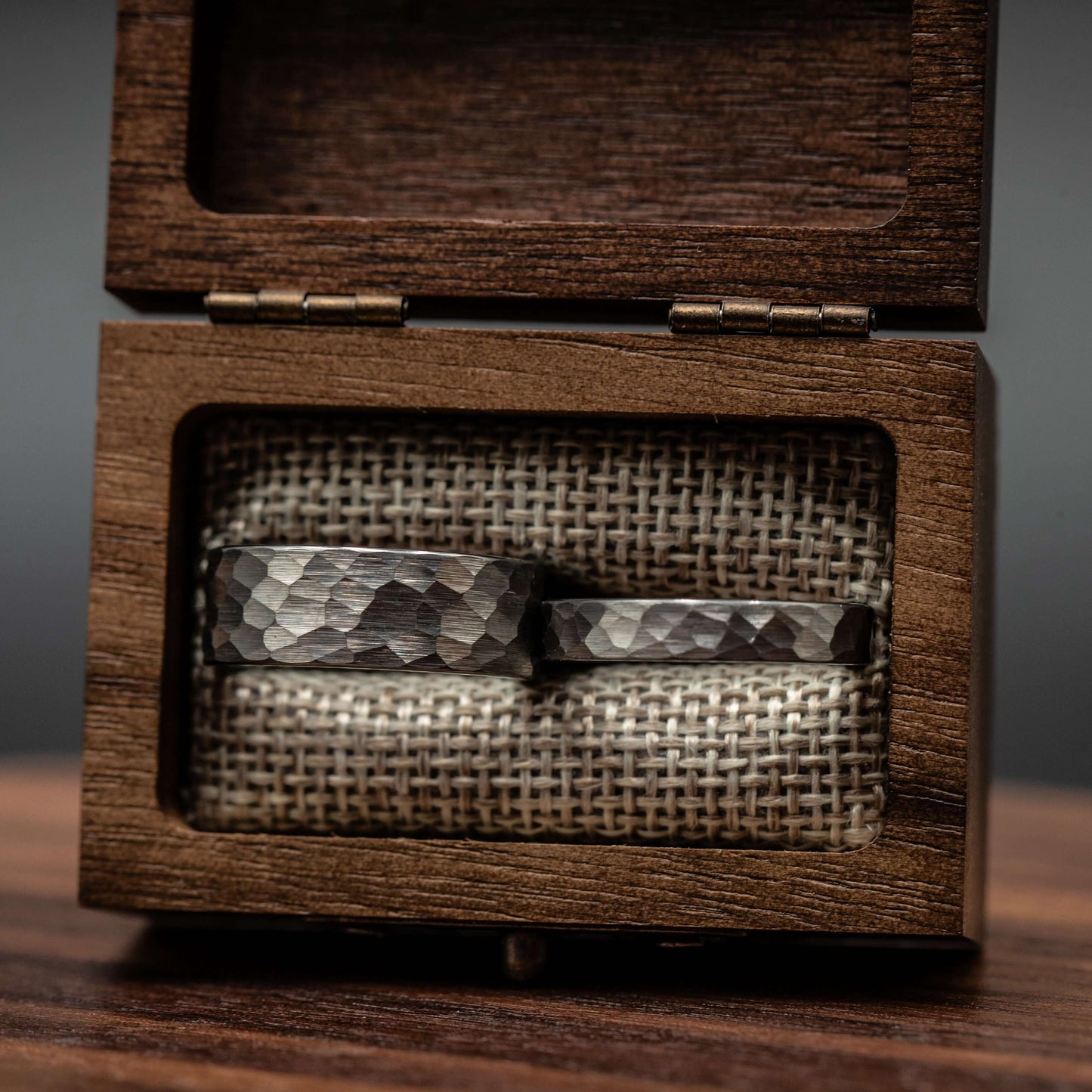 Couples hammered silver wedding rings displayed in a wooden box with a burlap interior.