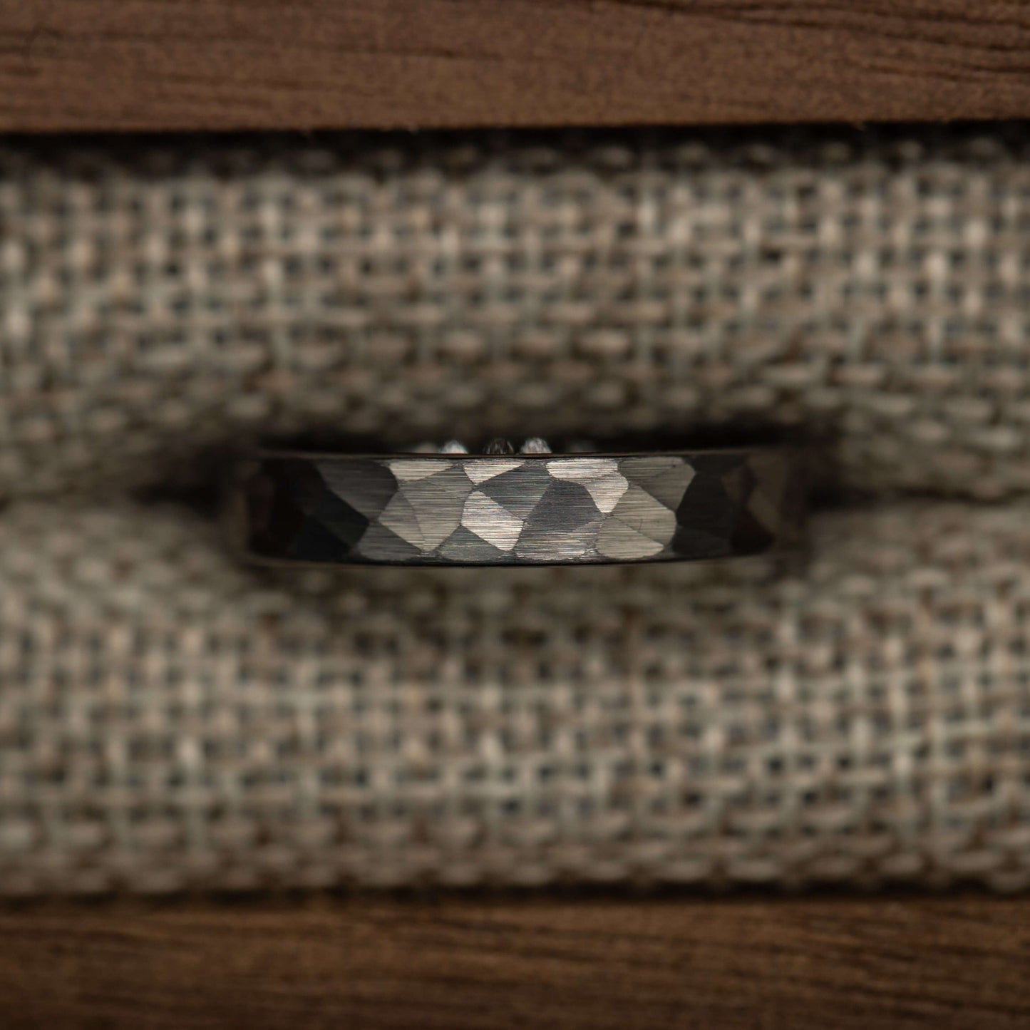 Hammered silver tungsten wedding band with a unique faceted design, displayed on a textured fabric background.