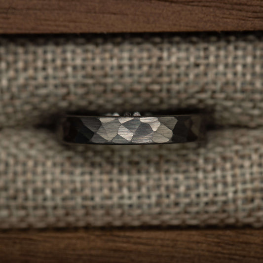 Hammered silver tungsten wedding band with a unique faceted design, displayed on a textured fabric background.