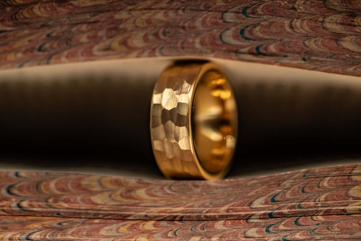 Men's 8mm width 18k Yellow Gold tungsten wedding ring standing on its die in between pages of a book