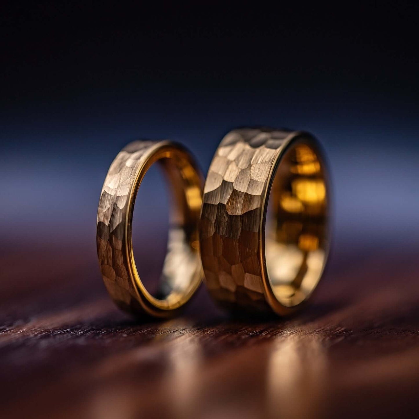 Couple's Wedding ring Set Yellow Gold 8mm and 4mm Tungsten rings with Hammered finish standing side by side on a wooden table