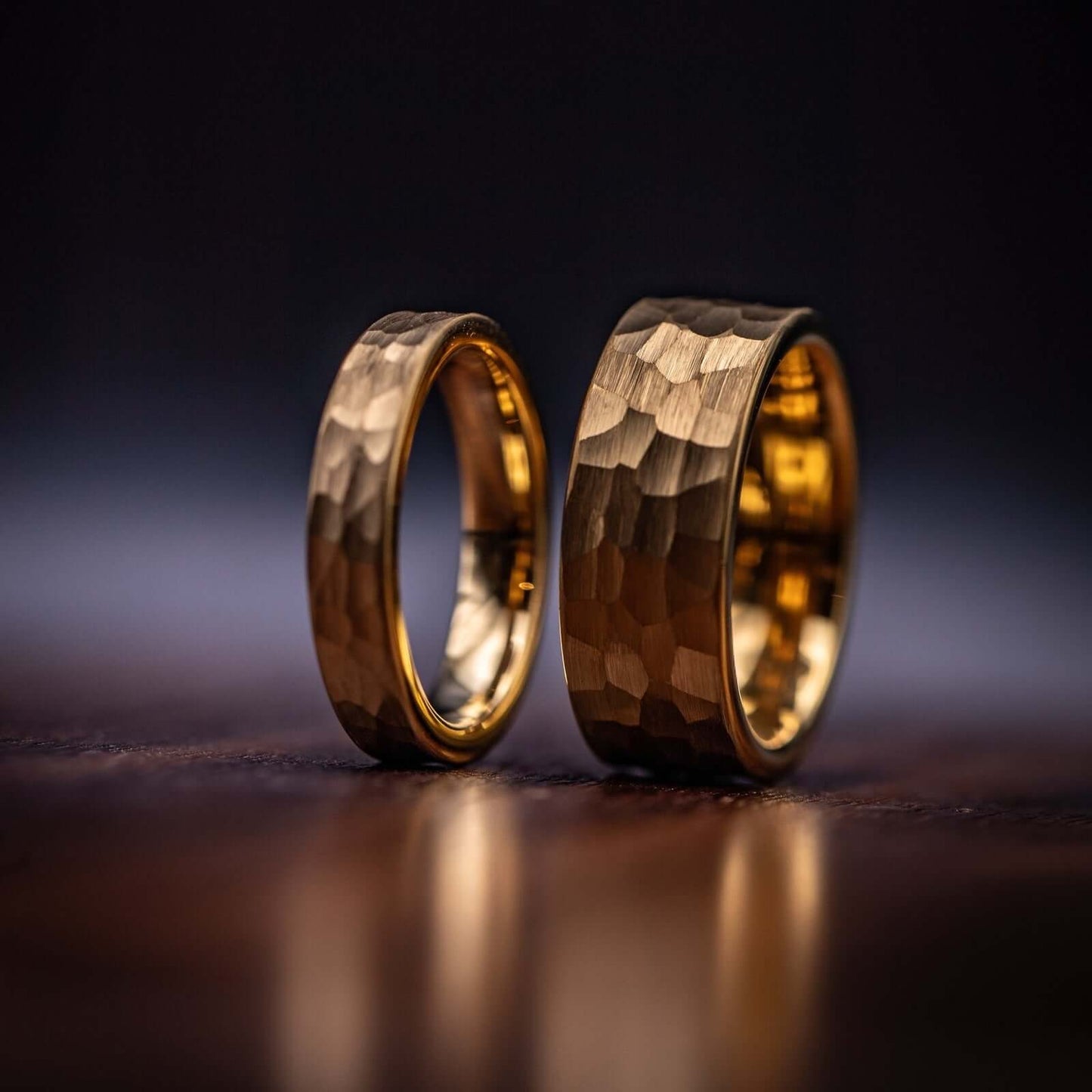 Couple's Wedding ring Set Yellow Gold 8mm and 4mm Tungsten rings with Hammered finish standing side by side on a wooden table