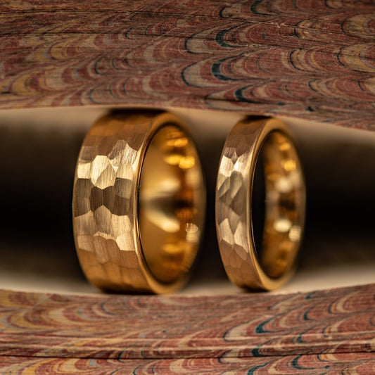 Couple's Wedding ring Set Yellow Gold 8mm and 4mm Tungsten rings with Hammered finish standing side by side in between pages of a book
