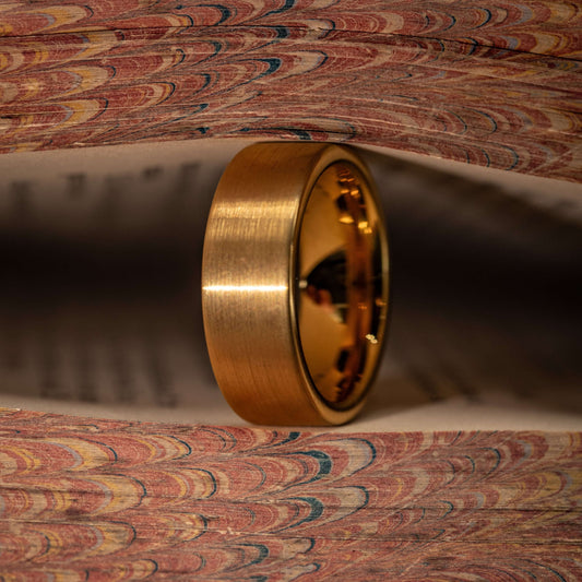 Gold brushed wedding ring displayed between pages of a decorative book, showcasing its unique design and finish.