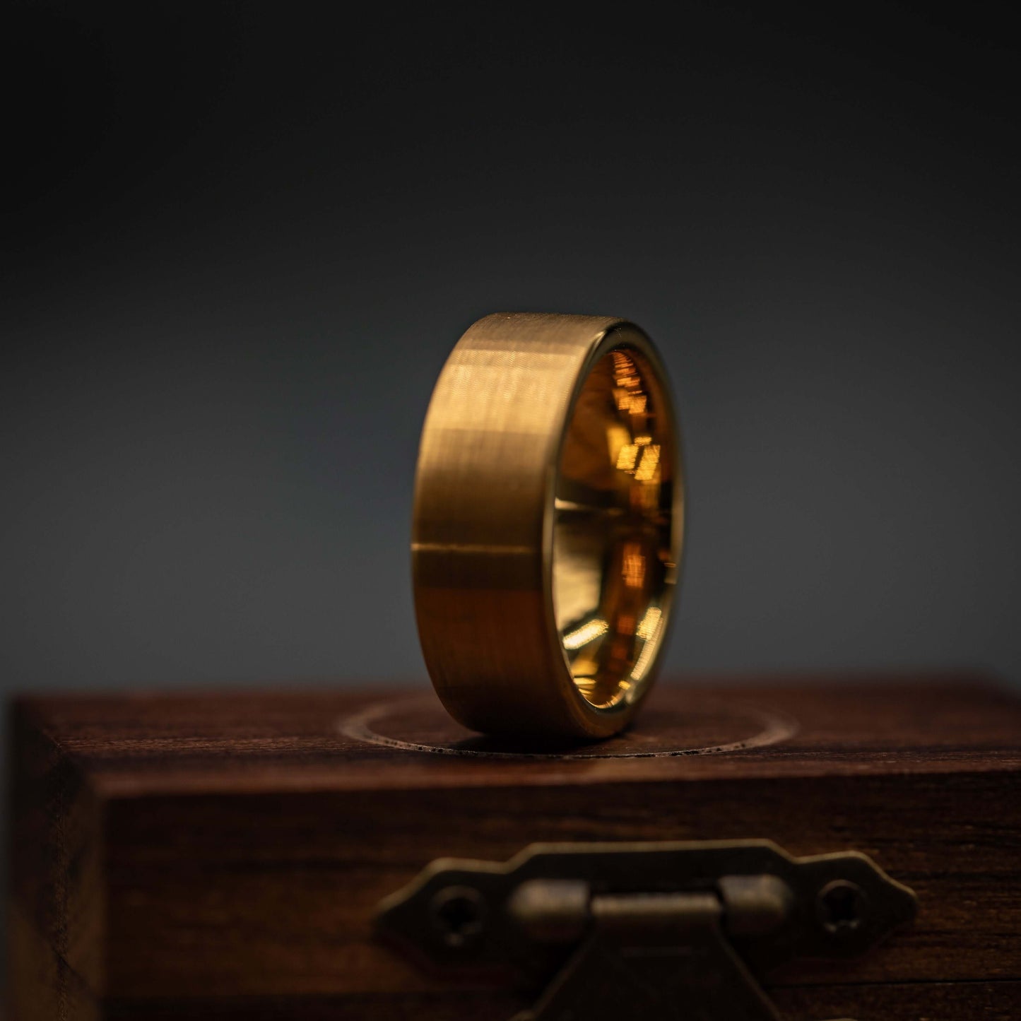 Gold brushed tungsten wedding ring displayed on a wooden box, highlighting its unique design and yellow gold finish.