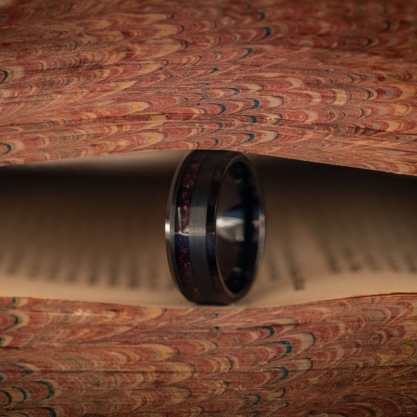 Black brushed tungsten ring featuring black fire opal, set against an artistic backdrop of vintage book pages.