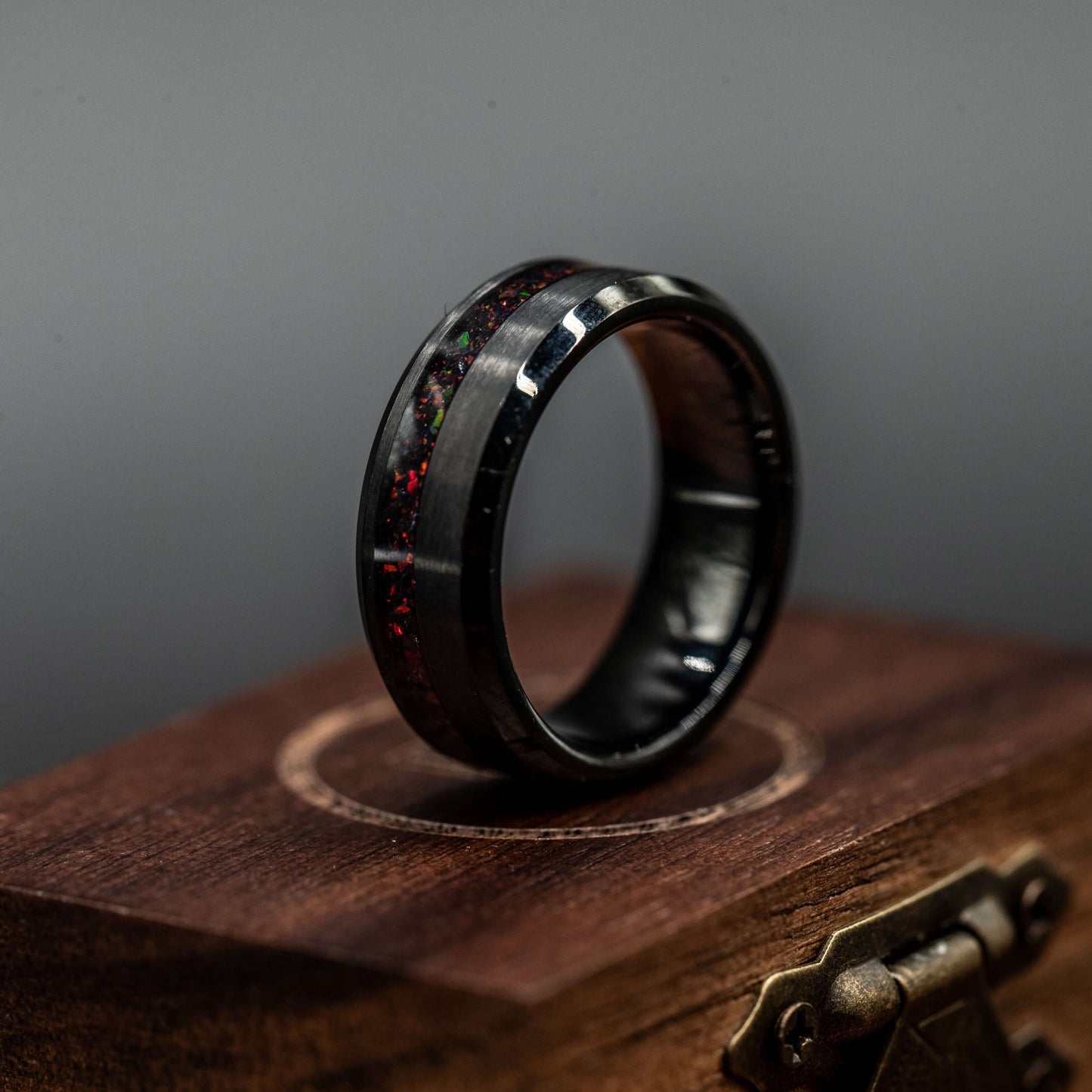 Black brushed tungsten ring with black fire opal channel, displayed on a wooden box. Unique men's wedding band.
