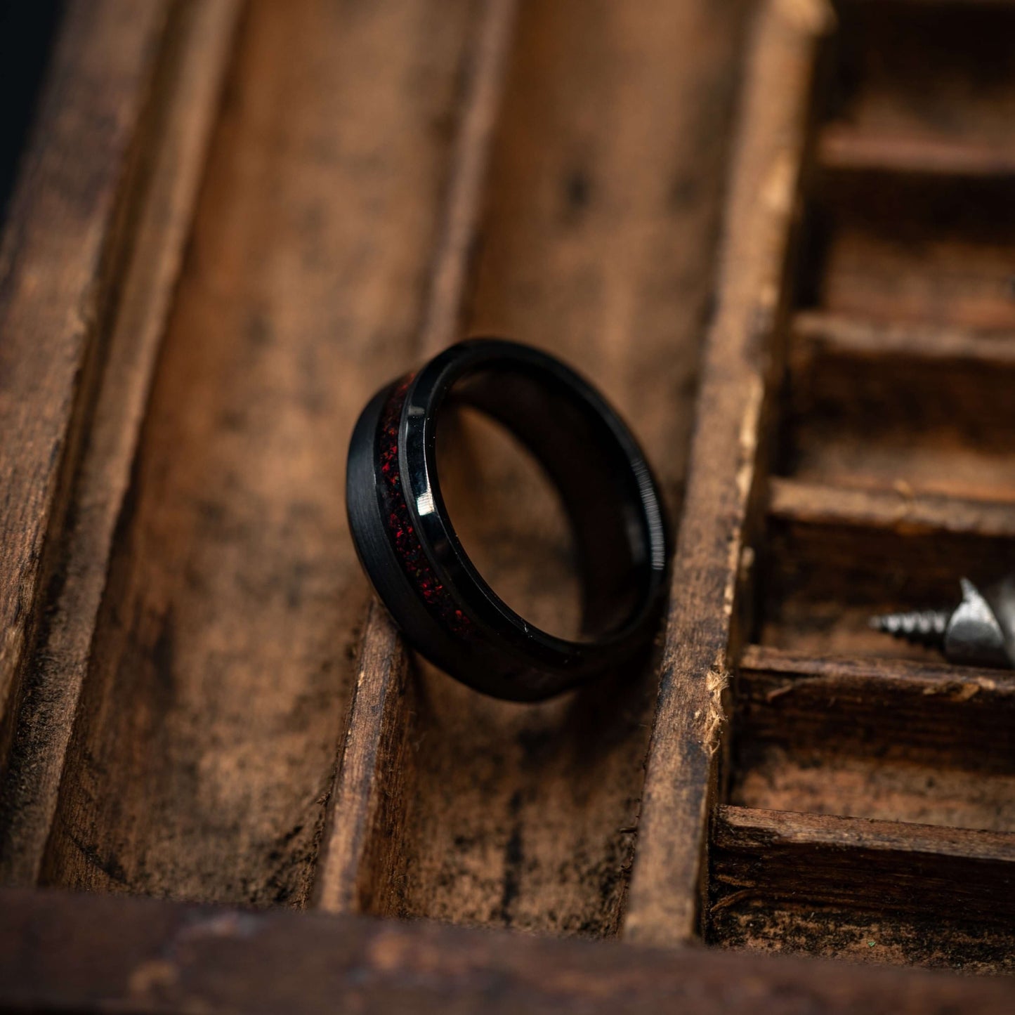 Black brushed tungsten ring with fire opal channel, resting on a wooden surface, showcasing its unique design.