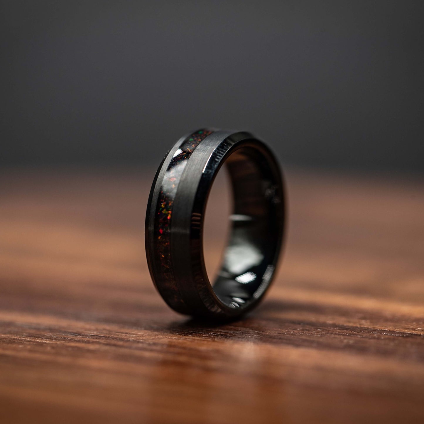 Black brushed tungsten ring with black fire opal channel, 8MM wide, modern men's wedding band on wooden surface.