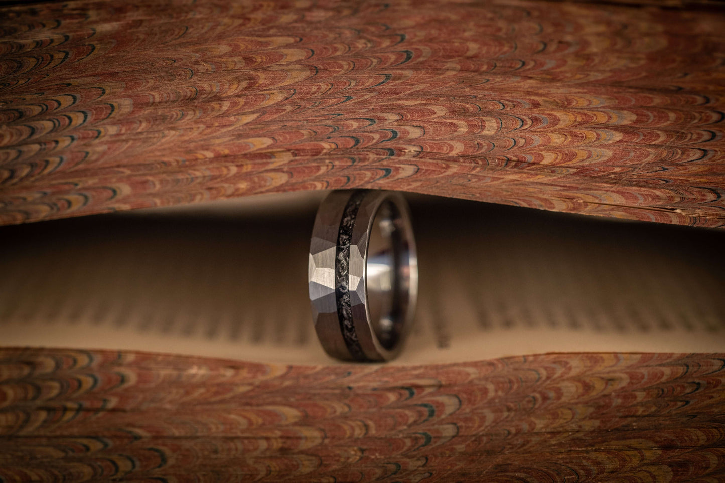 Hammered silver meteorite wedding band displayed on vintage book pages, highlighting its unique inlay and texture.