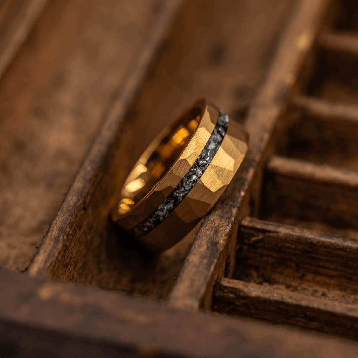 Men's yellow gold ring with hammered finish and silver meteorite inlay leaning in wooden box