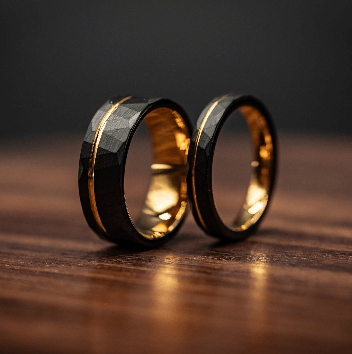 Couples hammered black wedding rings with yellow gold interior, unique textured bands for men and women, displayed on a wooden surface.