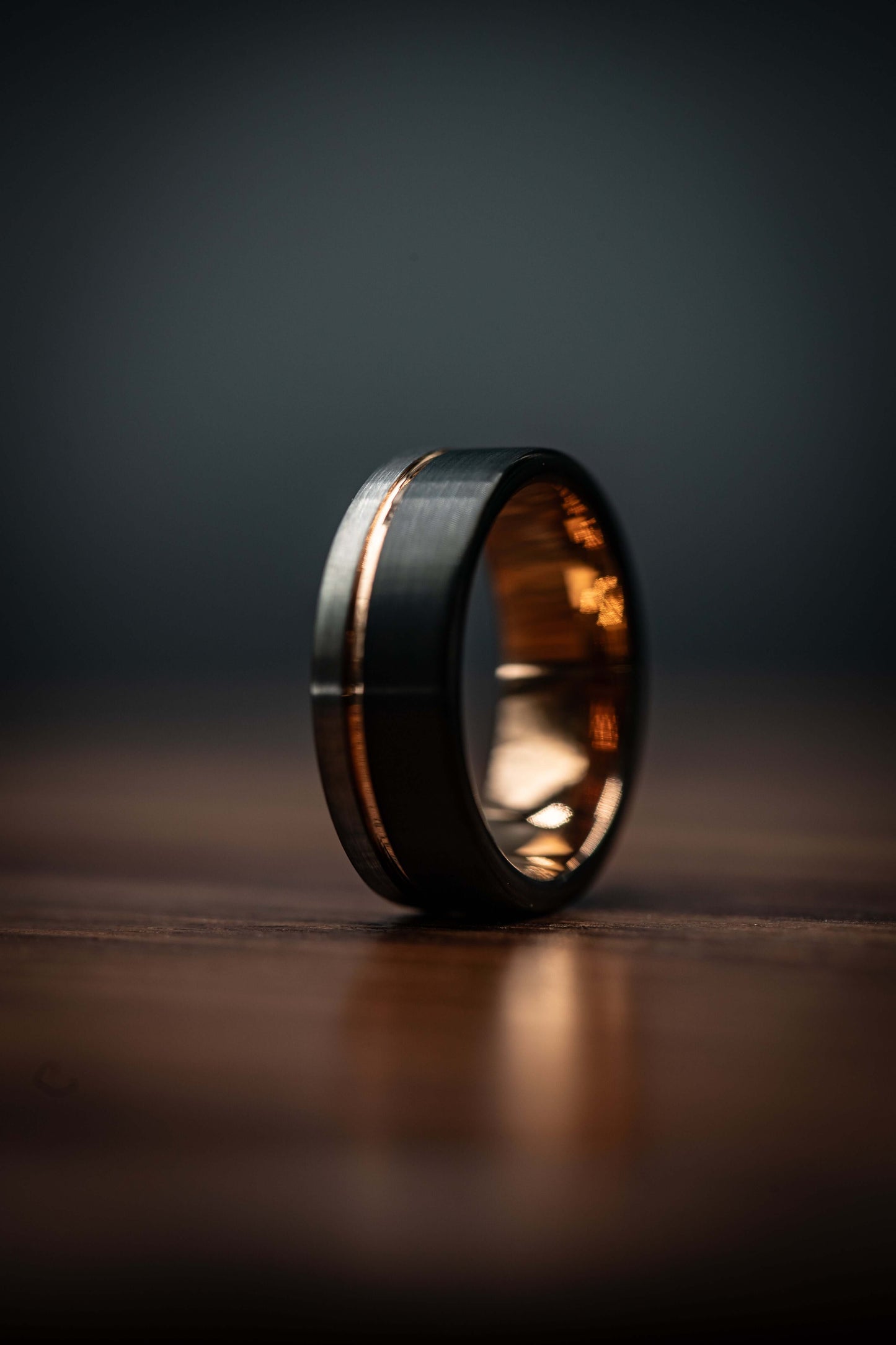 Black and silver wedding ring with rose gold inlay, unique hammered design, men's wedding band on wooden surface.