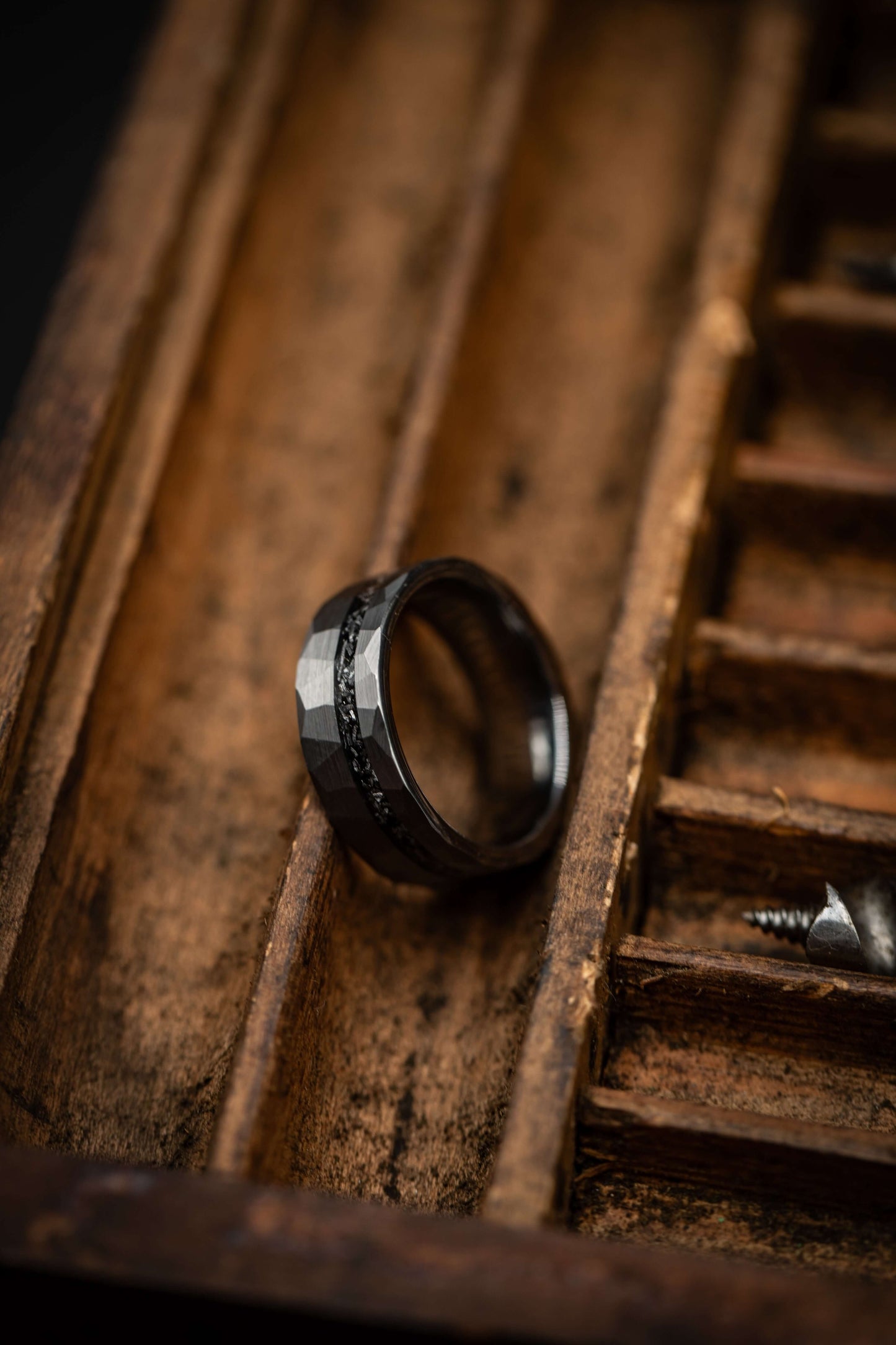Black hammered wedding band resting in a wooden box with a rustic finish.