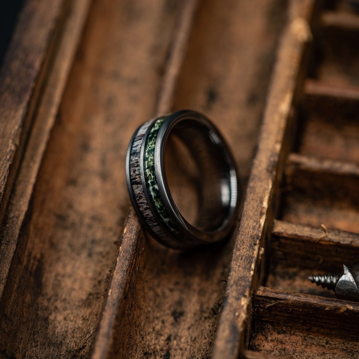 Men's deer antler and moss agate wedding band displayed on a wooden surface, highlighting the polished silver tungsten design.