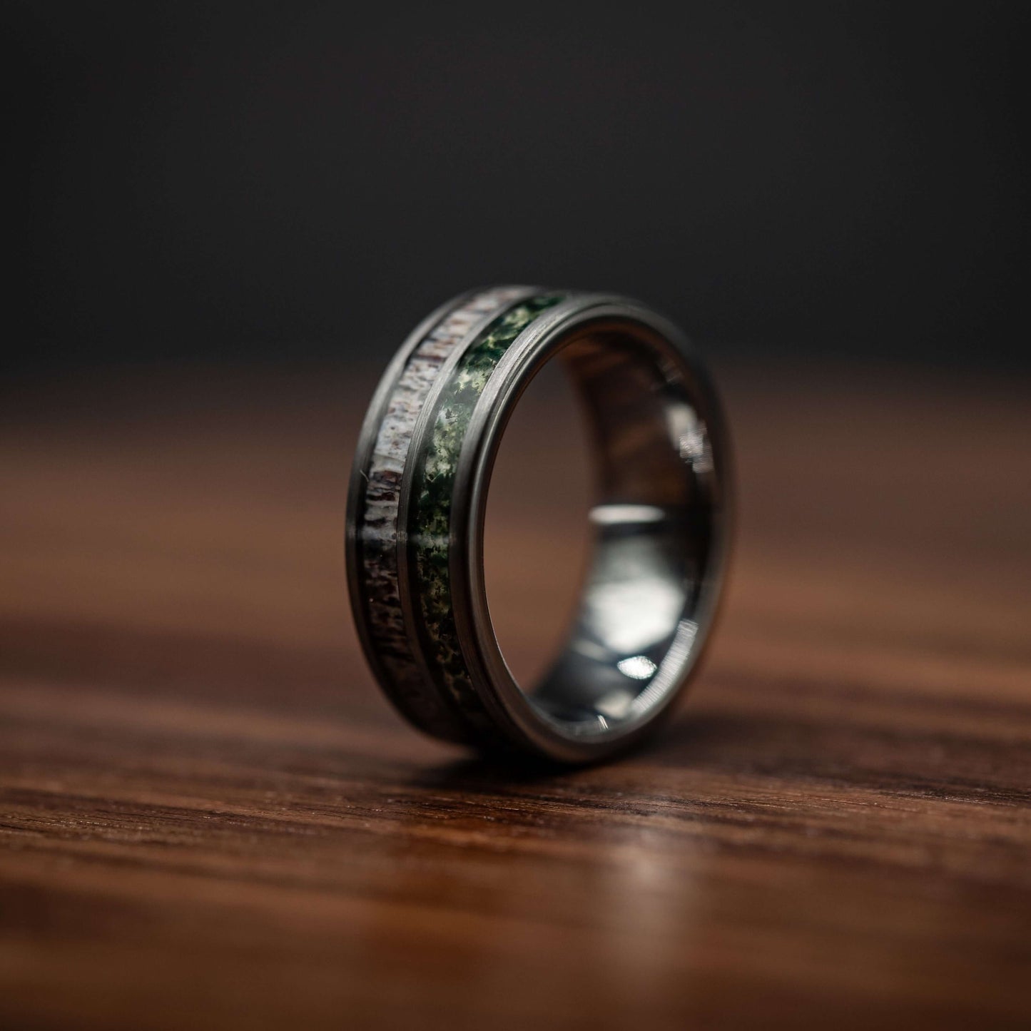 Men's deer antler and moss agate wedding band in polished silver tungsten, 8mm width, resting on a wooden surface.