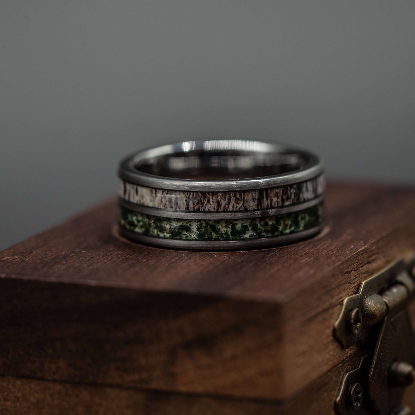 Deer antler and moss agate ring displayed on a wooden box, showcasing its polished silver tungsten band.