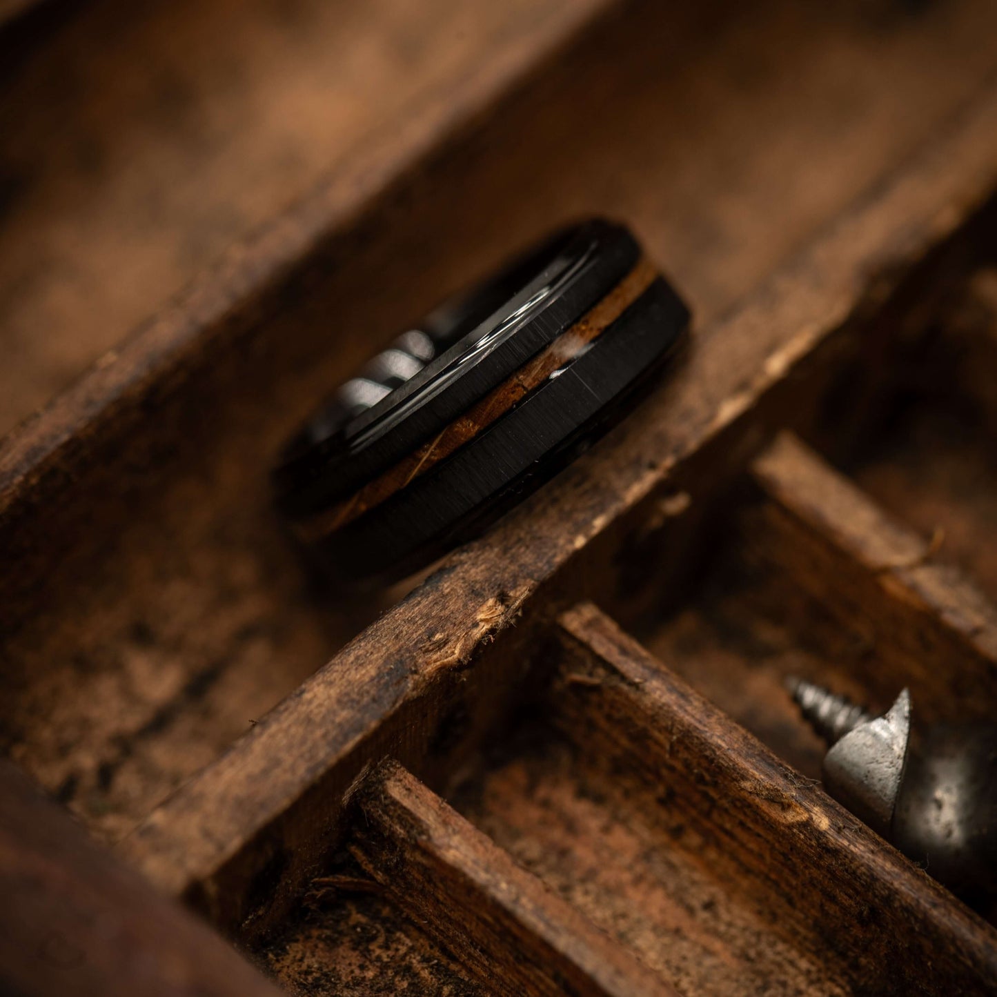 Black brushed tungsten and Koa wood wedding ring resting on rustic wooden surface.