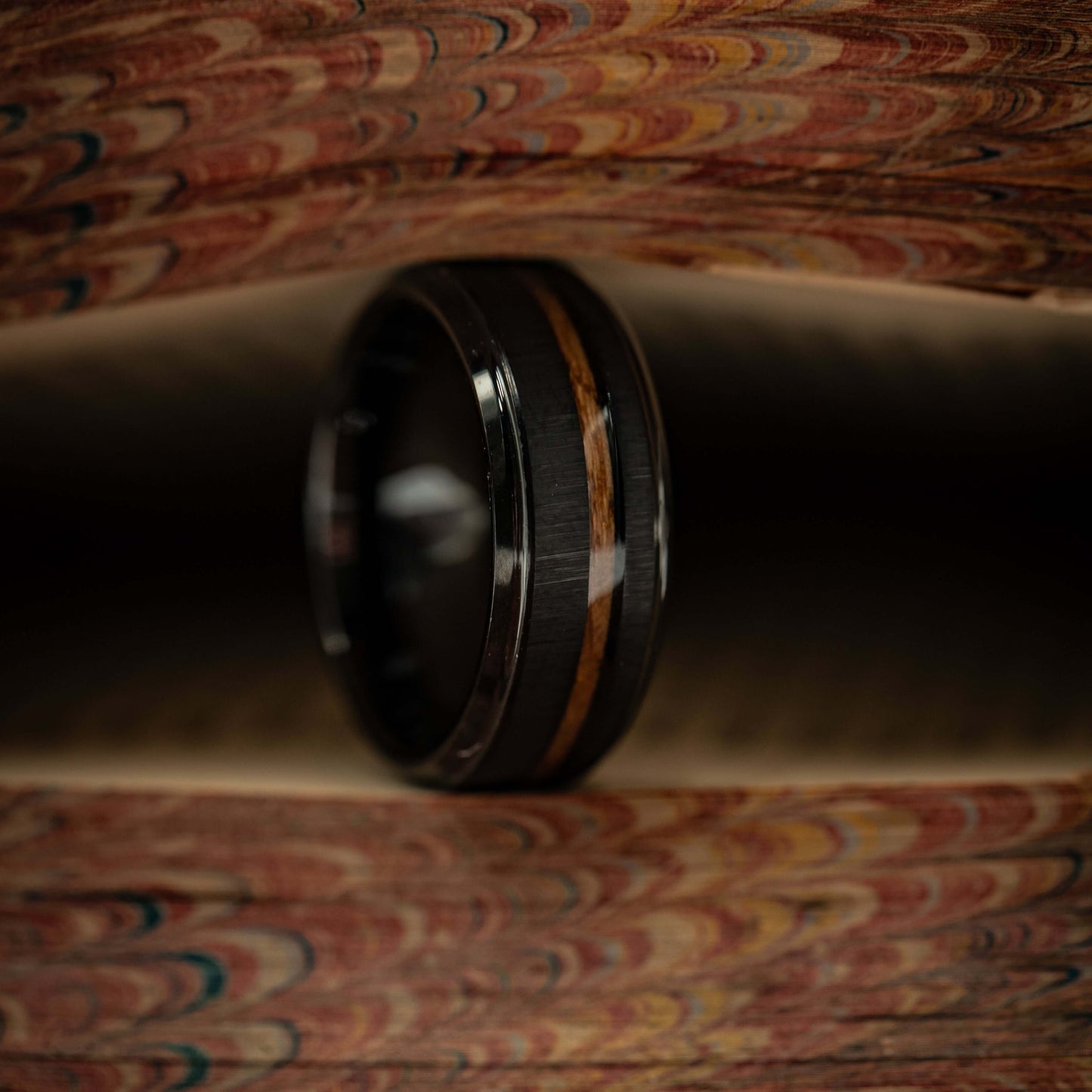 Black brushed tungsten and Hawaiian Koa wood wedding ring displayed on a textured surface.