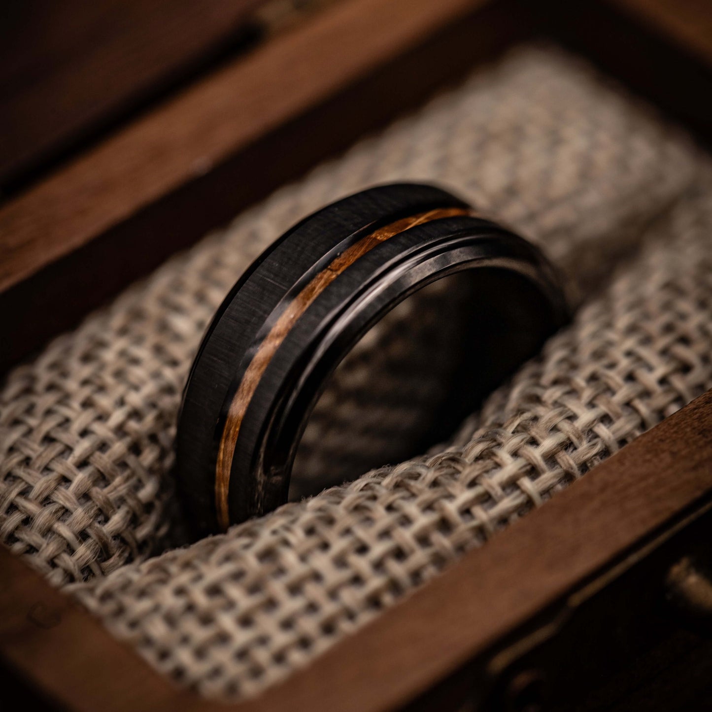 Black brushed tungsten and Hawaiian Koa wood ring in wooden box with textured fabric.