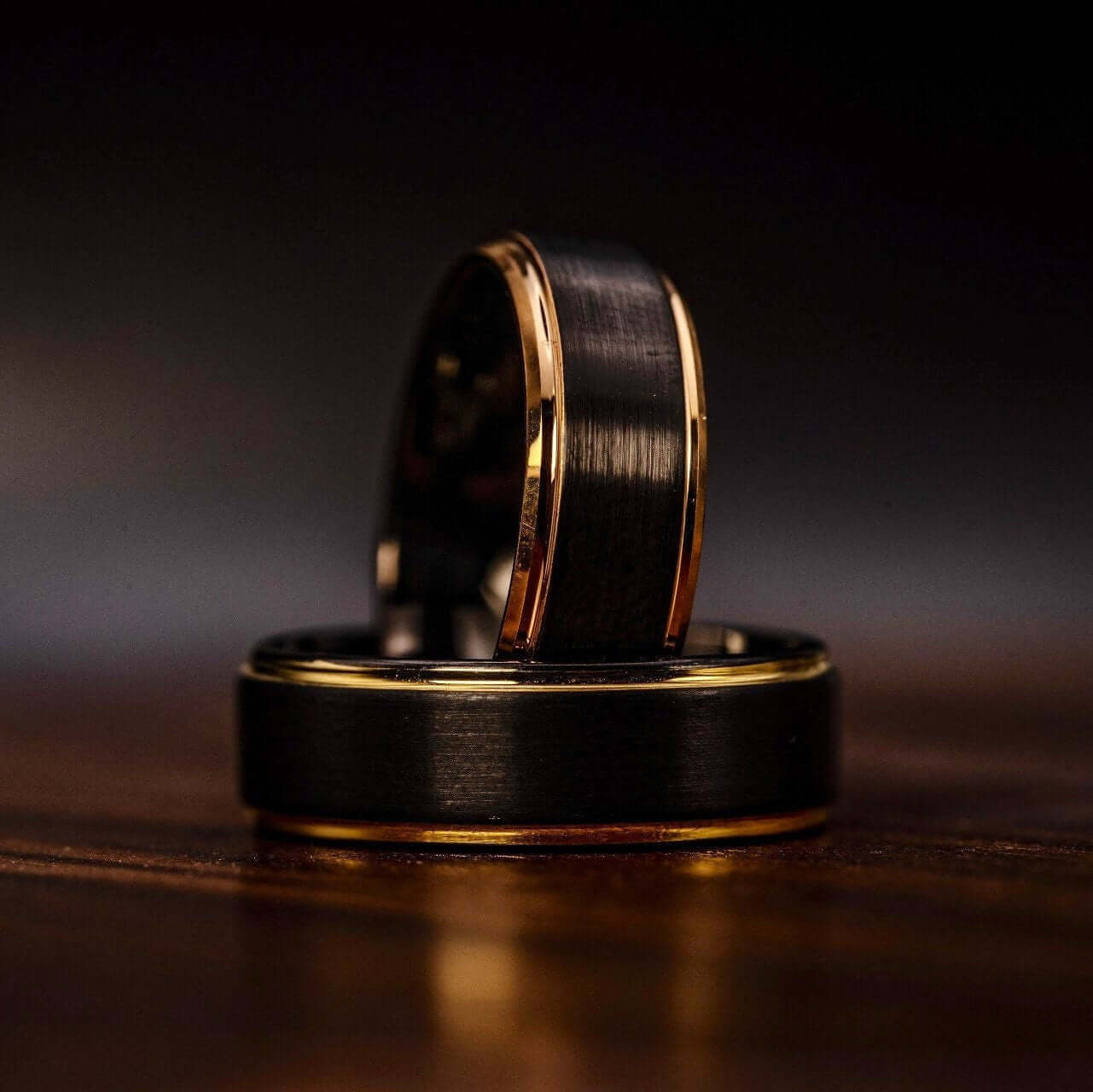 Black tungsten wedding ring with 18k Yellow Gold Step edges laying down with rose gold edge ring standing in inner loop
