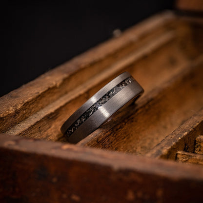 Men's 8mm Silver Tungsten wedding Band with meteorite inlay laying on its side in an old wooden box