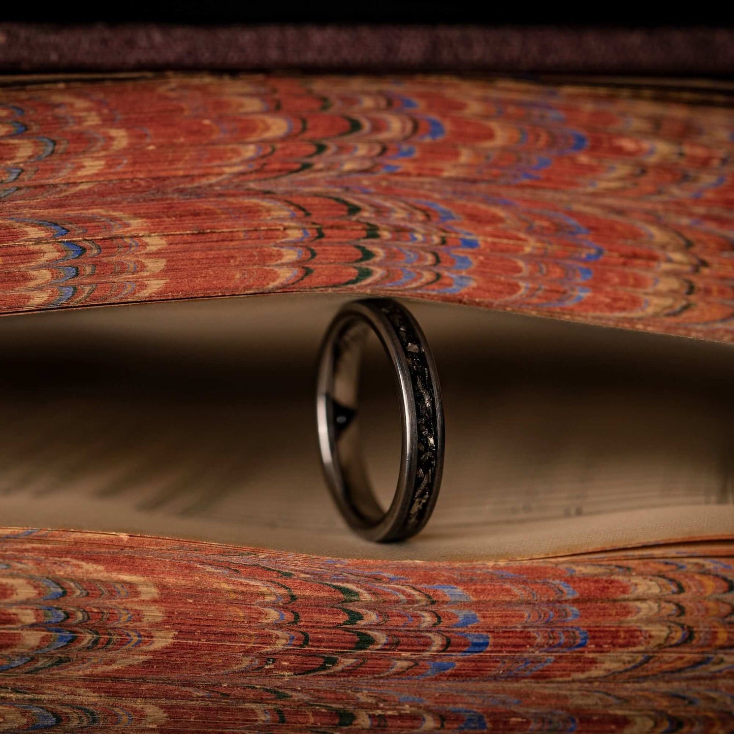 Women's 4mm silver tungsten wedding ring standing on its side between the pages of a book