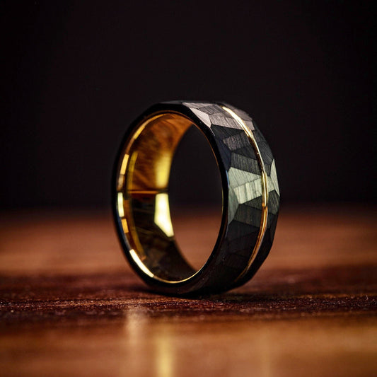 Men's hammered black wedding ring with yellow gold accents, offering a unique look.