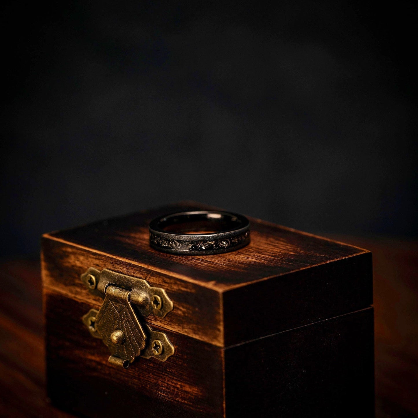Women's Black Tungsten Wedding Ring with Meteorite inlay and Sandblasted finish laying on its side on top of walnut ring box