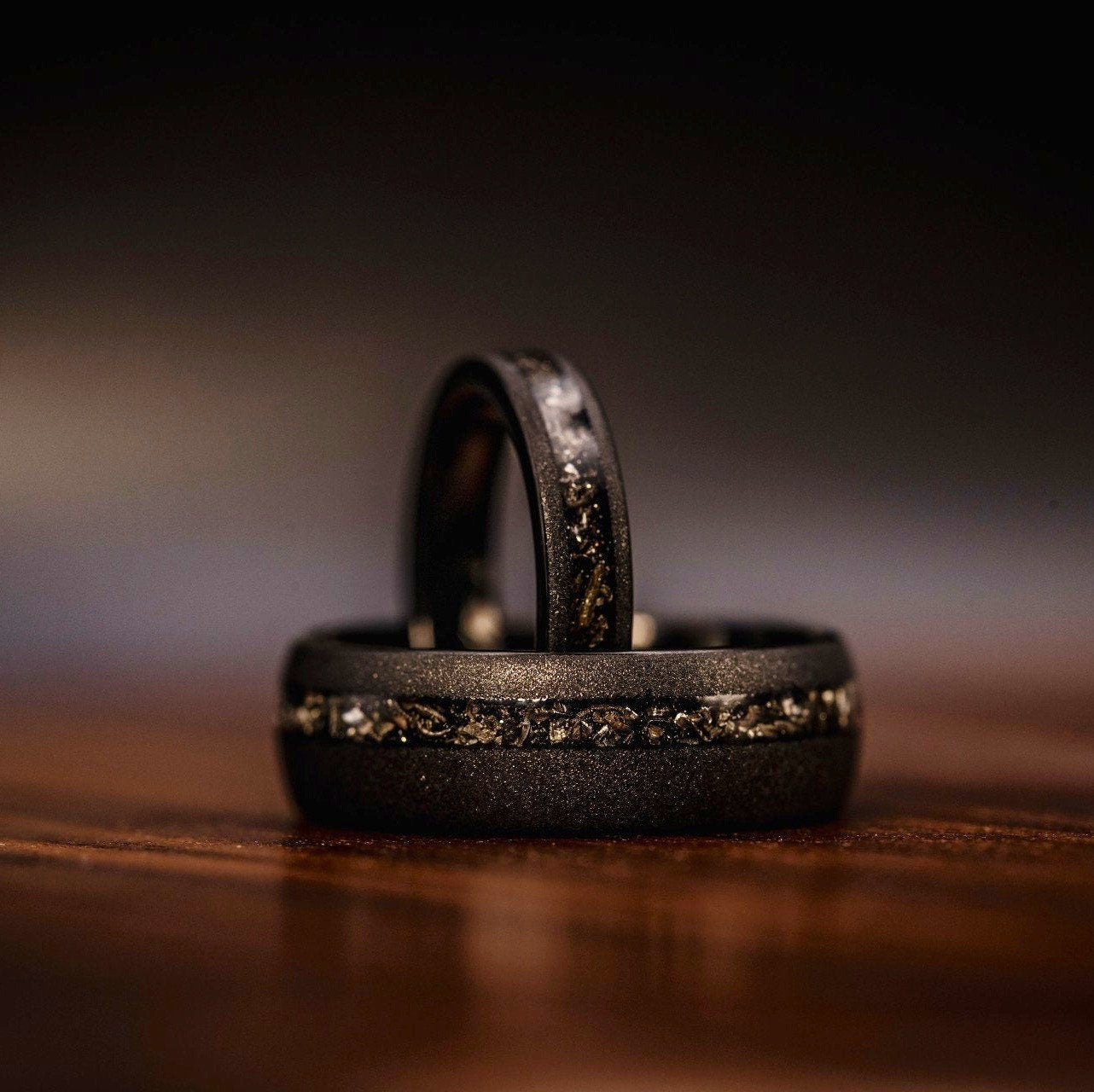 Women's Black Tungsten Wedding Ring with Meteorite inlay and Sandblasted finish standing inside of mens 8mm ring