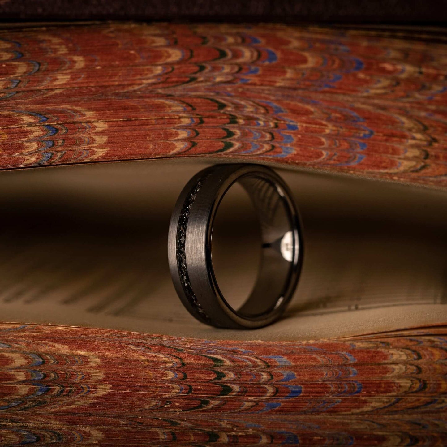 Men's 8mm Silver Wedding ring with Meteorite inlay standing on its side in between pages of a book